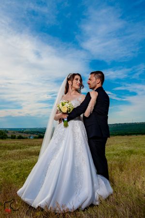 A romantic wedding portrait captured in a serene meadow landscape with mountains in the distance.