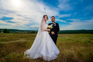 Wedding couple embracing in an open field with dramatic cloud formations overhead.