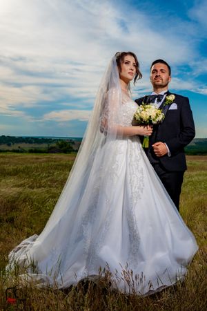 Elegant bridal portrait featuring a flowing white dress against natural grassland scenery.