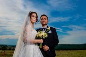 Romantic wedding moment captured in a sun-lit field with scenic mountain views.