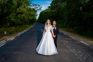 A couple in formal wedding attire poses on a tree-lined country road on their special day.