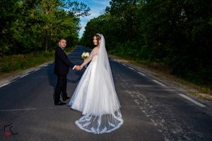 Newlyweds share a romantic moment on a quiet country road with trees lining both sides.