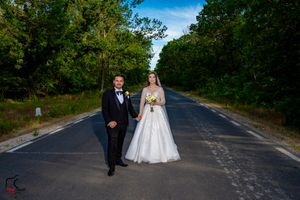 Wedding couple poses in the middle of a scenic tree-lined road on a sunny day.
