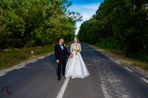 Bride in white gown and groom stand together on an empty rural road during their photoshoot.