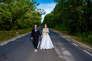 Wedding couple poses in formal attire on a peaceful country road surrounded by greenery.