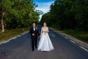 Bride in flowing white dress and groom pose on empty rural road for wedding photos.