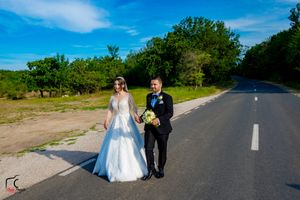 Wedding couple stands on a sunny country road with natural greenery in the background.
