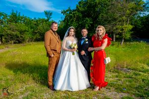 Wedding party members gather outdoors against a backdrop of lush greenery and blue skies.