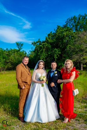 Wedding party in formal attire poses together in a grassy field on a sunny afternoon.
