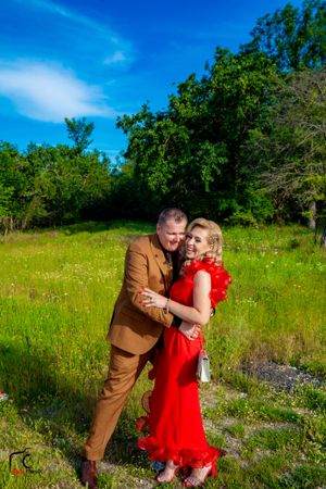 Two people in contrasting brown and red outfits share a playful moment in a meadow.