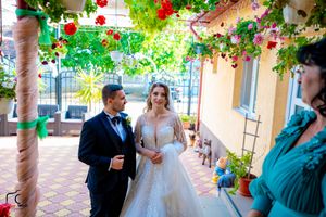 Wedding ceremony takes place under a floral-covered pergola with hanging decorations.