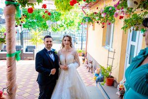 A wedding celebration takes place under a beautiful pergola adorned with red flowers and lush greenery.