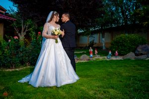 A bride in a flowing white gown and groom share an intimate moment in a garden setting.