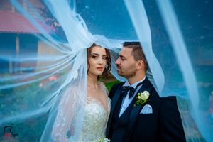 A dramatic wedding portrait with flowing veil against a turquoise background.