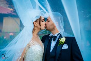 Romantic wedding moment captured under billowing white veil with ethereal blue lighting.