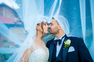 Ethereal wedding portrait with flowing veil against blue-tinted background.