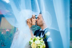 Wedding couple shares tender moment under flowing veil with yellow bouquet.