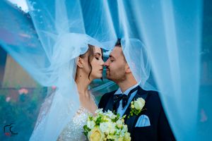 Romantic wedding moment captured with flowing veil and yellow bouquet against blue backdrop.