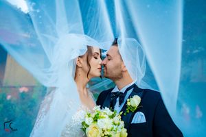 Romantic wedding portrait with flowing veil against blue sky backdrop and white floral bouquet.