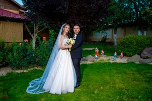 Wedding couple poses in garden setting with white dress and black suit among greenery.
