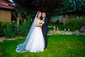 Elegant wedding photo in lush garden with long veil trailing behind couple.