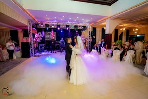 A couple shares their first dance on a misty dance floor illuminated by purple and blue lights at an elegant reception venue.