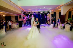 A romantic first dance moment captured in a ballroom with dramatic lighting and fog effects on the dance floor.
