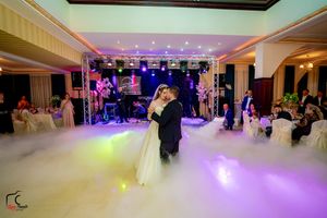 Newlyweds dance surrounded by atmospheric fog and colorful stage lighting in an elegant reception hall.