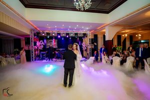 A couple dances beneath a crystal chandelier on a fog-covered dance floor with concert-style lighting setup.