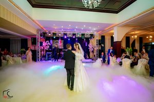 A wedding couple's silhouette dances in a cloud of fog with purple ambient lighting in an elegant ballroom.