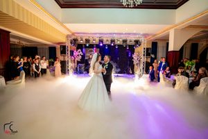 A couple's dance moment captured in a fog-filled ballroom with dramatic lighting and watching guests.