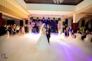A couple shares their first dance at an elegant wedding reception with purple lighting and fog effects on the dance floor.