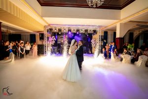 Newlyweds dance in a beautifully lit ballroom with purple stage lighting and white fog effects.