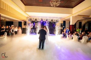 A misty dance floor illuminated with purple lights and an elegant archway setup for a wedding reception.