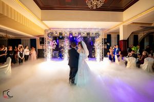 Couple dancing in an elegant ballroom with dramatic purple lighting and fog effects during their wedding reception.