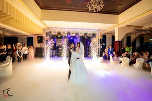Couple dances beneath chandeliers in an elegant ballroom with purple lighting and atmospheric effects.