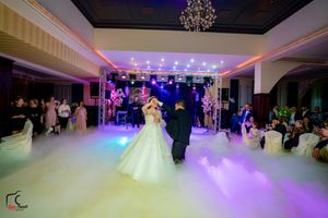 Couple dancing in a fog-filled ballroom with purple ambient lighting and elegant decor.