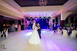 Spacious ballroom decorated with ambient lighting and fog effects for wedding celebration.