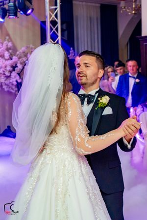 Couple sharing their first dance on a misty dance floor with dramatic purple lighting.