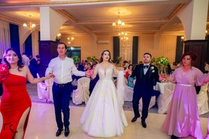 Wedding party members dance in a line formation at an elegant ballroom reception with purple lighting.