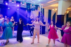 Wedding guests dance in a circle on a white dance floor with blue stage lighting and professional sound equipment.