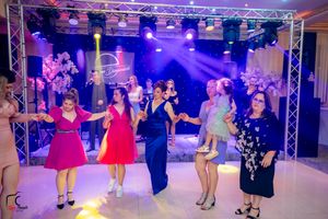 Wedding guests dance in formation under purple stage lights and professional lighting equipment.