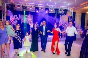 Wedding celebration features guests dancing in formation under dramatic purple stage lighting.