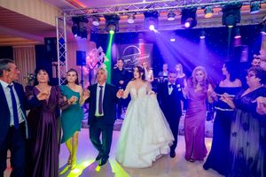 Formal celebration with guests dancing under purple theatrical lighting in an elegant ballroom setting.