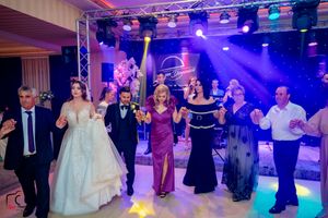 Guests in formal attire dancing in a line at a wedding reception with purple stage lighting.