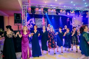 Wedding guests dancing in a line under purple stage lighting at an evening reception.