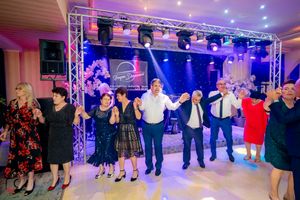 Dancers in formal attire move in unison under professional stage lighting at an indoor celebration.