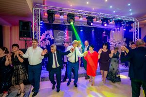 Celebratory group dance with participants in formal wear under vibrant purple and blue stage lighting.