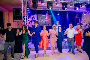 Party guests dancing in a line on a dance floor with colorful stage lighting and professional sound equipment.
