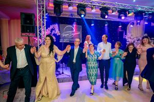 Guests holding hands in a traditional dance line at an elegant event with professional lighting.